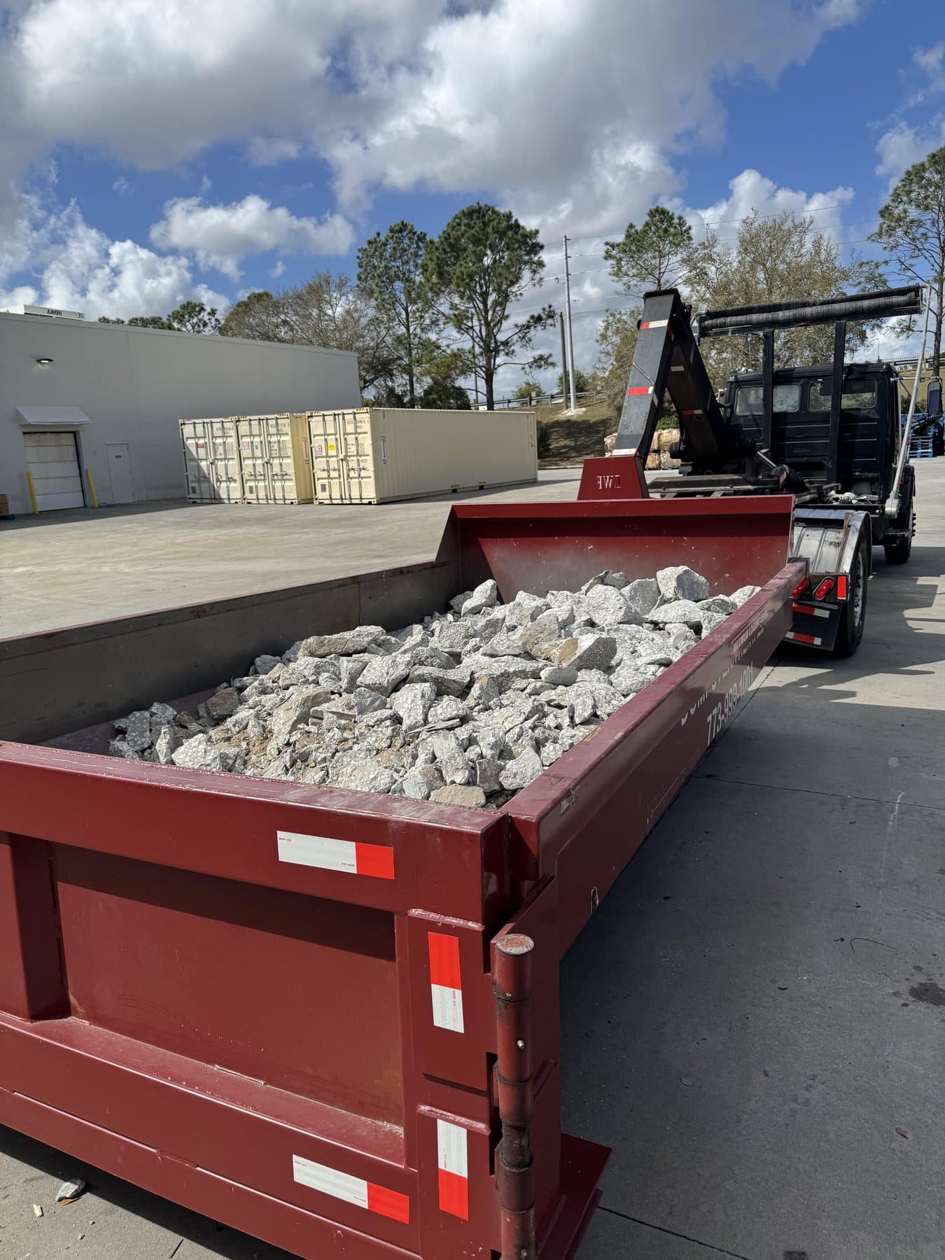 10 yard DumpsterX dumpster loaded with concrete, hooked to the roll-off truck